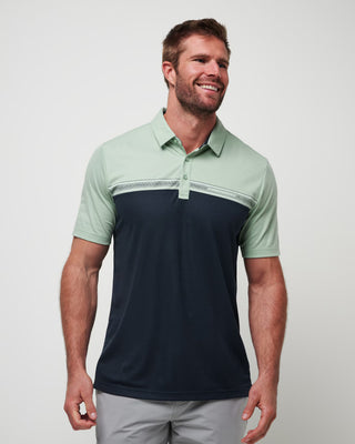 A man wearing a color-blocked polo shirt with the upper part in green and the lower part in navy blue. The shirt has a collar and a button-up front.