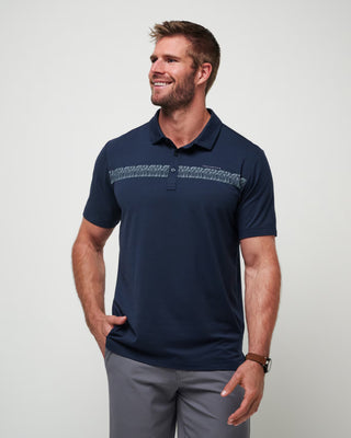 A man wearing a navy blue performance polo shirt with a geometric chest stripe design and short sleeves.