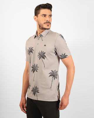 Man wearing a beige polo shirt with palm tree patterns on a white background